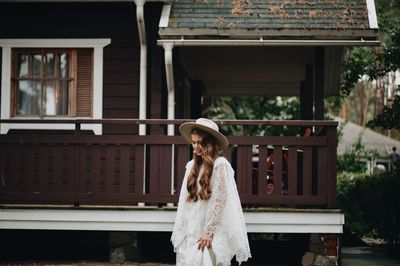 Bride wearing hat while standing against house