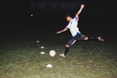 Full length of man playing soccer on field at night