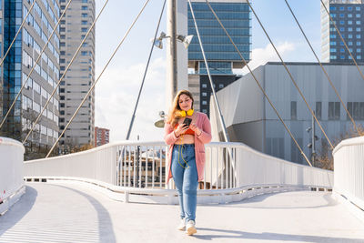 Full length of woman using mobile phone on bridge