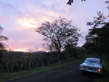 Car on road amidst field against sky during sunset