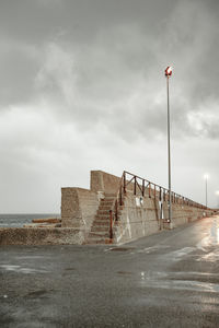 Low angle view of illuminated street light by surrounding wall against cloudy sky at dusk