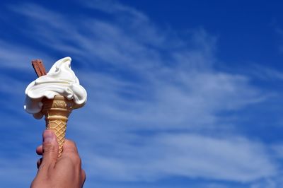 Low angle view of hand holding ice cream against blue sky