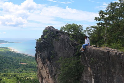 People on rock amidst trees against sky