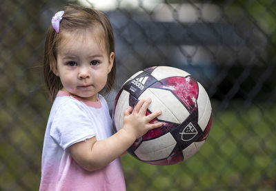 Portrait of cute girl holding ball while sitting on soccer field