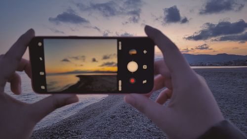 Midsection of person using mobile phone against sky during sunset