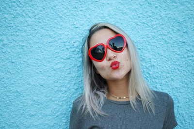 Young woman wearing heart shape sunglasses against blue wall