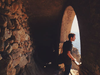 Side view of young man looking through arch window from cave