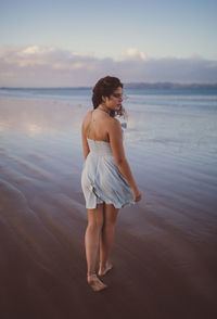 Woman standing on beach against sky during sunset