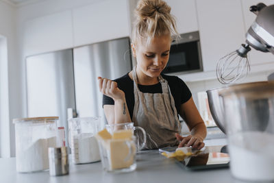 Young woman checking cell phone in kitchen while baking