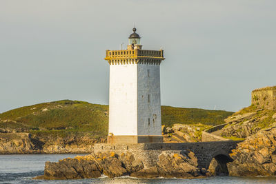 Lighthouse by building against sky