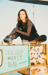 Portrait of young woman sitting on retaining wall