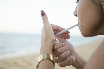Close-up of woman smoking marijuana joint against sea and sky