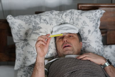 Man checking temperature while lying on bed at home