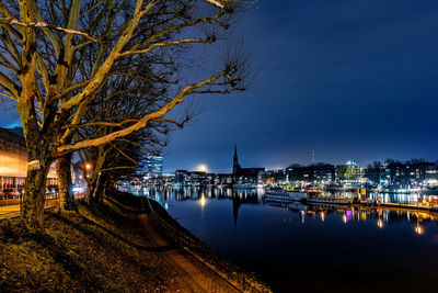 Illuminated buildings by river against sky at night