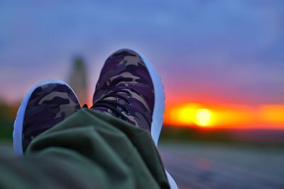 Low section of person sitting against sky during sunset