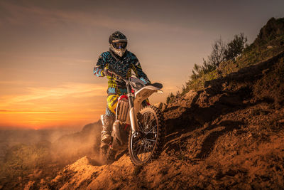 Man riding motorcycle on mountain against sky during sunset
