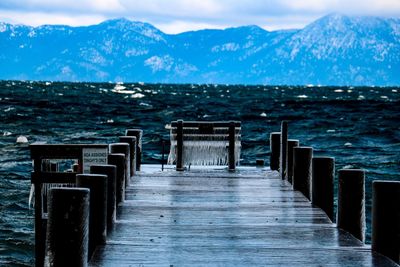 Wooden pier on sea by mountains against sky