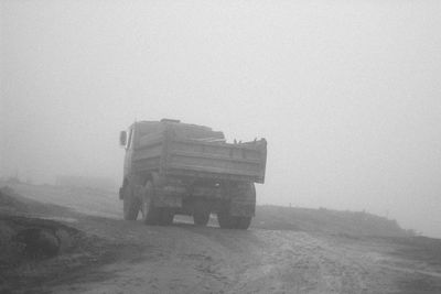 Road amidst field against sky during foggy weather