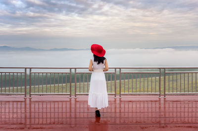 Rear view of woman standing on railing against sky