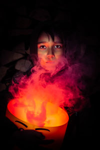 Portrait of young woman holding cigarette against black background