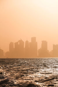 Silhouette buildings by sea against clear sky during sunset