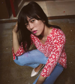 High angle portrait of young woman with bangs crouching at home