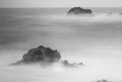Long exposure shot of rock formation in sea against sky