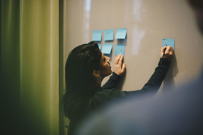 Rear view of businesswoman analyzing adhesive notes stuck on whiteboard in office