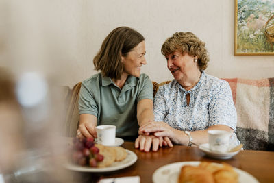 Smiling elderly woman talking with female nurse while having snacks at home
