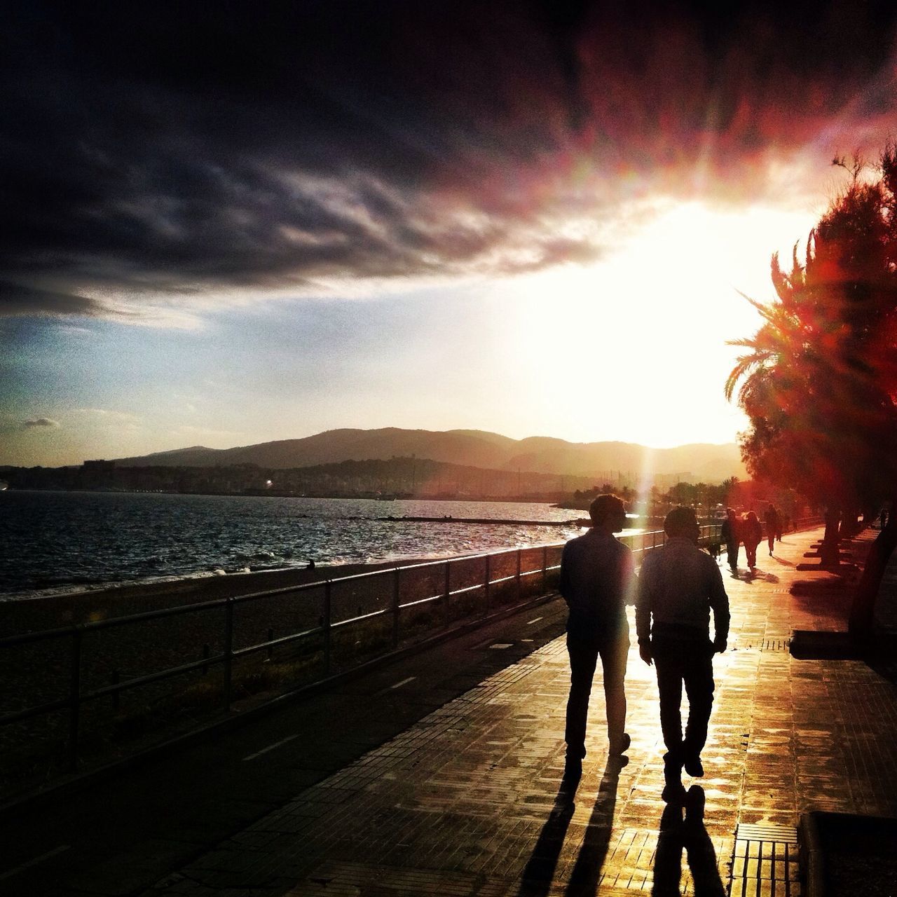 sunset, sun, lifestyles, sky, leisure activity, silhouette, men, water, person, sunlight, sunbeam, full length, walking, lens flare, sea, standing, cloud - sky, rear view