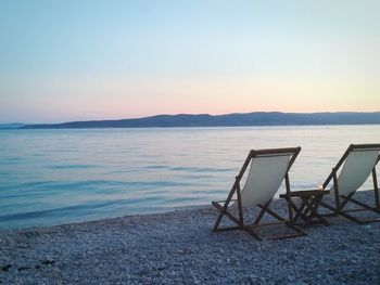 Chairs on beach against clear sky during sunset