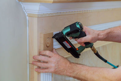 Close-up of man using nail gun on wall at home