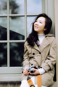 Portrait of young woman standing against window