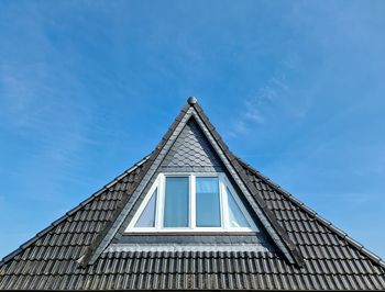 Roof window in velux style with black roof tiles against a blue sky