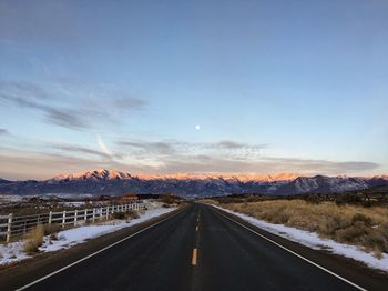 Road by snowcapped mountains against sky during winter