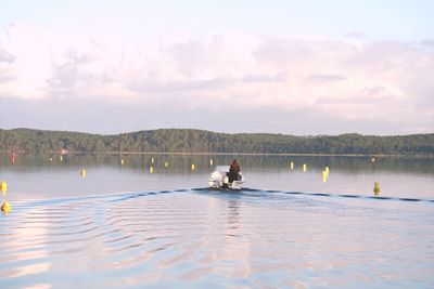 Rear view of man on boat at lake against sky