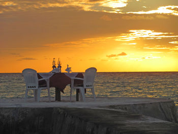 Chairs and tables on beach against sky during sunset