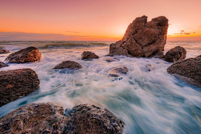 Rocks on beach against sky during sunset