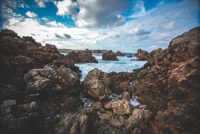 Rock formations by sea against cloudy sky