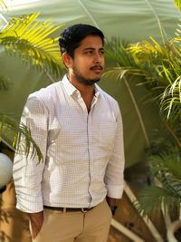 Young man looking away while standing amidst plants