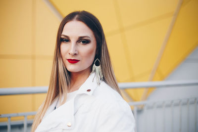 Portrait of young woman wearing earring against yellow building