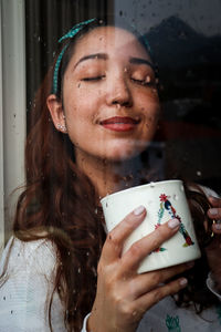 Smiling woman with eyes closed seen through window