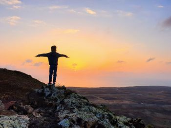 Man standing on rock against sky during sunset