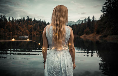 Rear view of woman standing in lake against sky