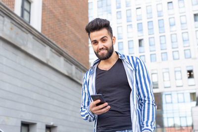 Young man using mobile phone while standing against office building