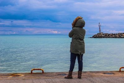 Rear view of woman standing on promenade against cloudy sky