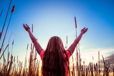 Rear view of girl with arms outstretched against cloudy sky