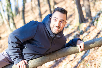 Young man smiling and joking with a fallen tree in the forest in winter