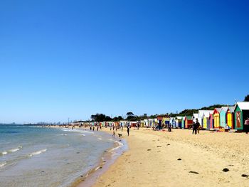 Group of people on beach against clear blue sky