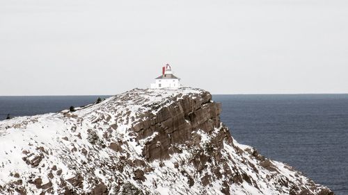 Lighthouse on cliff by sea against clear sky